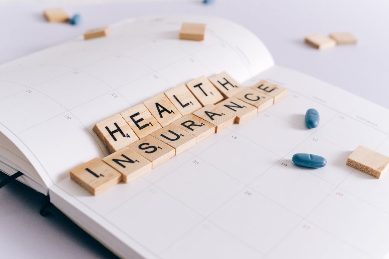 Scrabble tiles spelling Health Insurance on a calendar with pills.